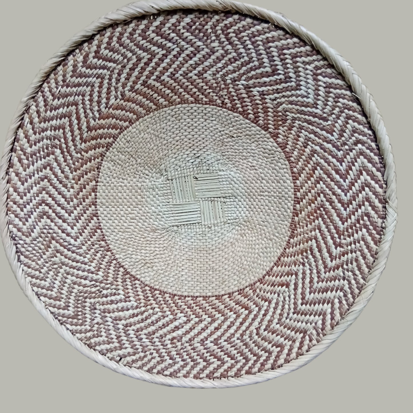 Round woven Malawian Tonga Basket with herringbone pattern on a wooden surface