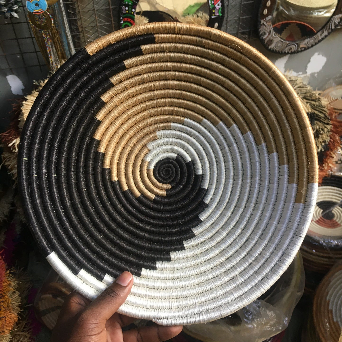 Handwoven basket with concentric circles held by a hand against a blurred background