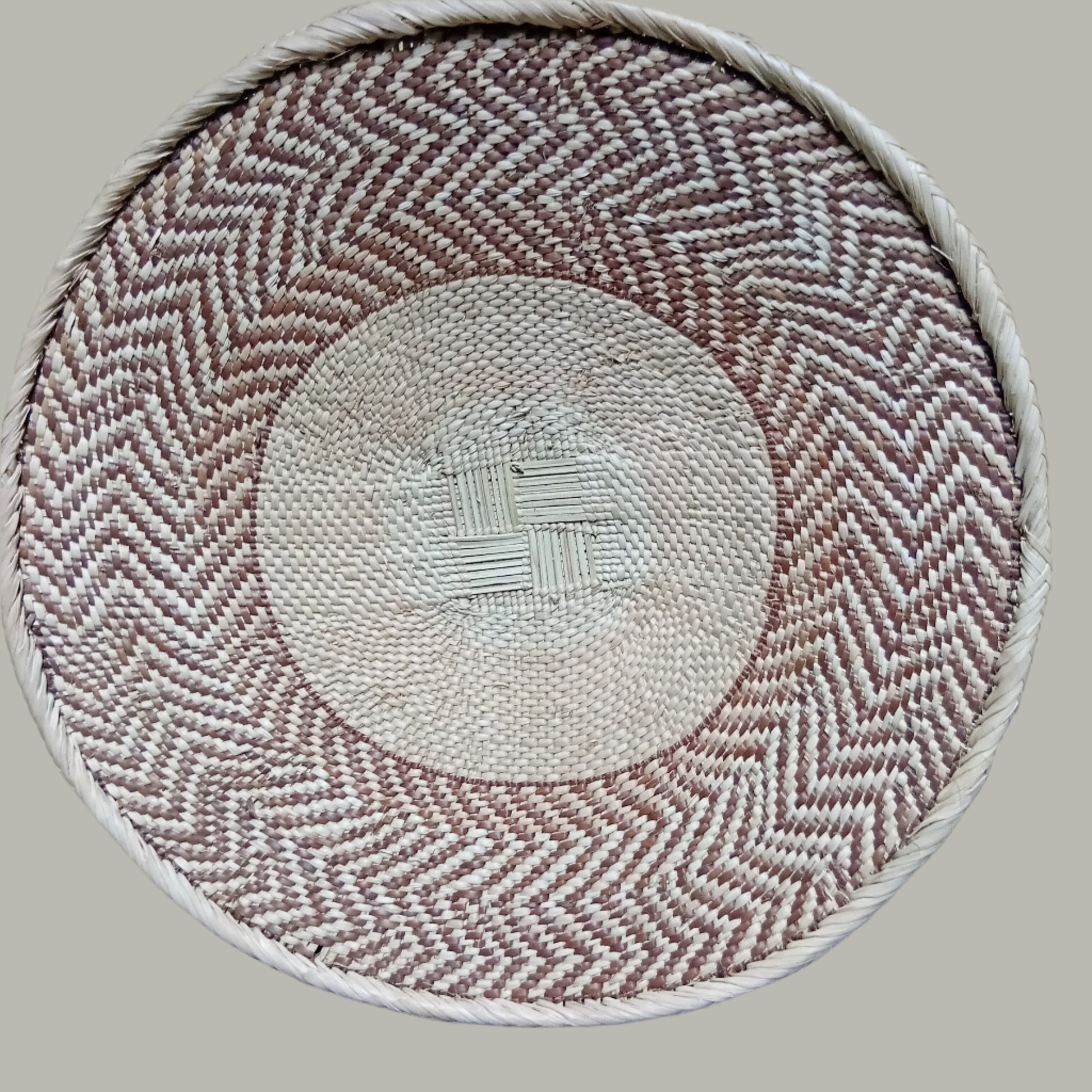 Round woven Malawian Tonga Basket with herringbone pattern on a wooden surface