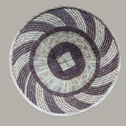 Round woven basket with concentric circle pattern on a wooden floor.