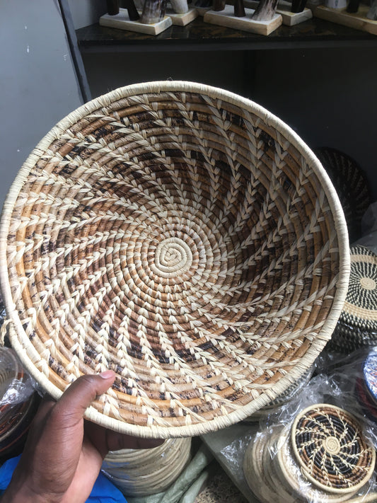 Hand-woven basket with a spiral pattern held by a hand, with other similar baskets in the background.