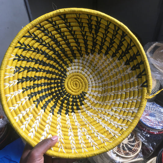 Yellow woven basket with black and white patterns held by a hand.