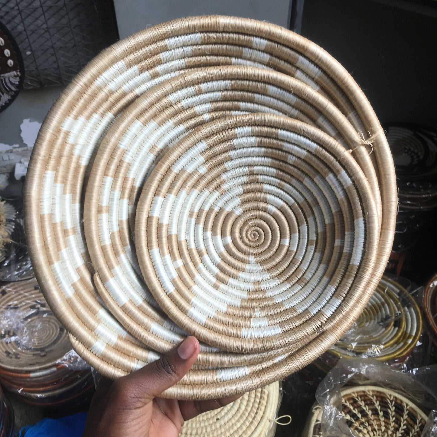 Handmade woven basket with concentric circles held by a hand, with more baskets in the background.
