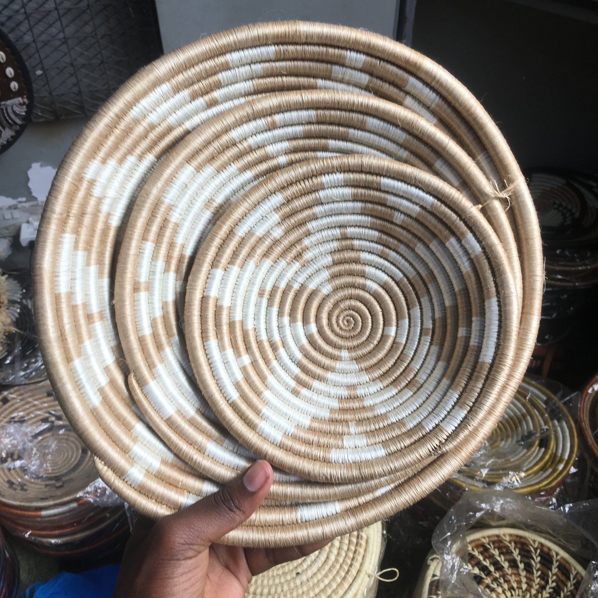 Handmade woven basket with concentric circles held by a hand, with more baskets in the background.