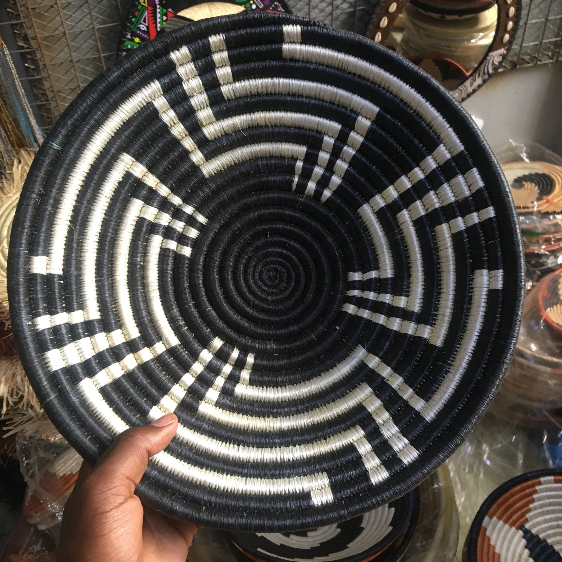 Hand holding a black and white woven bowl with intricate patterns.